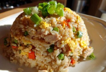 A mound of homemade chicken fried rice, featuring visible pieces of chicken, egg, peas, and carrots, topped with fresh green onions.