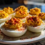 Close-up of several perfectly prepared deviled eggs sprinkled heavily with bright red paprika on a white plate.