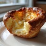 A close-up of a golden brown, tall yorkshire pudding with a bite taken out, showing its fluffy interior.