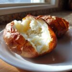 Close-up of a perfectly cooked air fryer baked potato, split open to show the fluffy white interior and crispy skin.