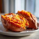 Close-up of a fluffy baked sweet potato, split open and sprinkled with coarse sea salt.
