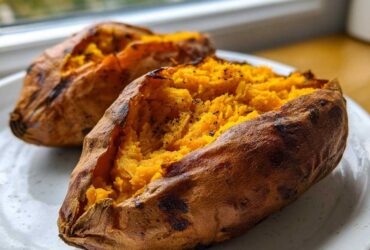 Two perfectly baked sweet potatoes, split open to show the fluffy, seasoned orange interior.