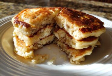 Close-up of a fluffy stack of banana pancakes cut in half, showing the moist interior texture.