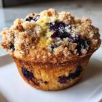 Close-up of a fluffy blueberry muffin featuring a golden-brown crumb topping and visible blueberries.
