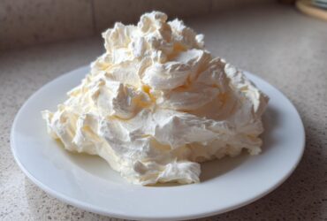 A generous, fluffy mound of freshly made cream cheese frosting piped onto a white plate.