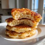 Close-up of a stack of four incredibly fluffy pancakes, cut open to show the airy interior, drizzled with syrup.