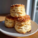 A stack of three incredibly fluffy scones, golden brown and topped with coarse sugar crystals, sitting on a white plate.