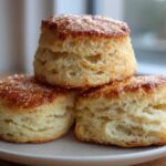 Three fluffy, tall scones stacked on a plate, featuring golden-brown tops sprinkled with coarse sugar.