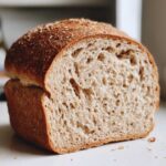 Close-up of a freshly baked whole wheat bread loaf cut in half, showing a fluffy, open crumb structure.