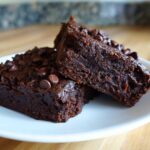 Two fudgy sweet potato brownies topped with chocolate chips resting on a white plate.