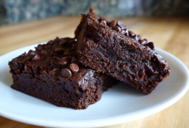 Two fudgy sweet potato brownies topped with chocolate chips resting on a white plate.