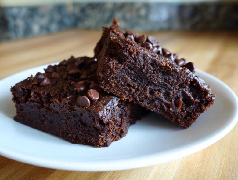 Two fudgy sweet potato brownies topped with chocolate chips resting on a white plate.