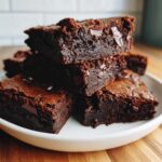 A stack of rich, fudgy sweet potato brownies loaded with visible chocolate chunks, served on a white plate.