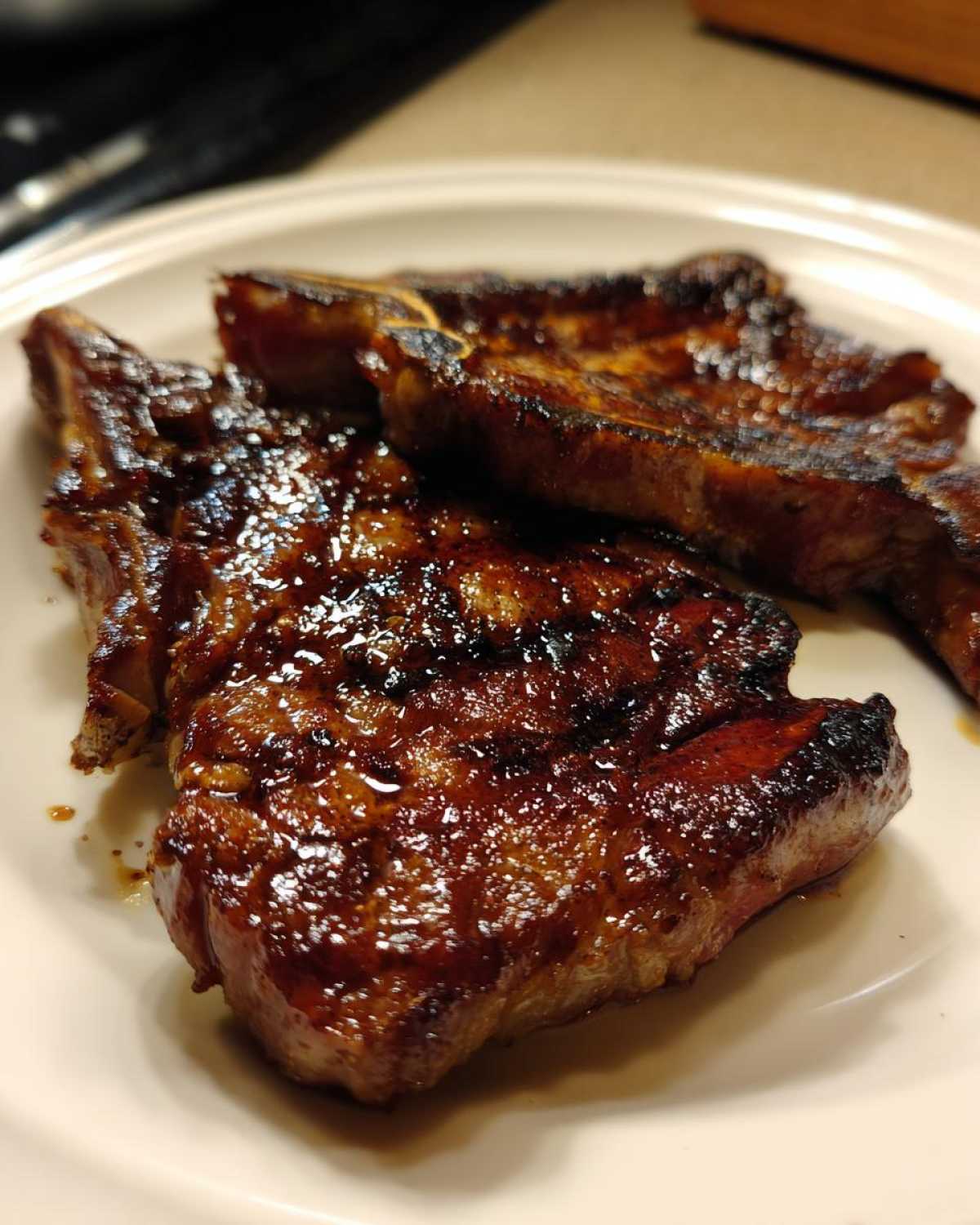 Two perfectly grilled and glazed pork steak recipe cuts resting on a light-colored plate.