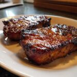Two thick, glazed pork steak pieces with a dark, caramelized crust served on a white plate.