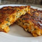 Close-up of two golden brown mashed potato cakes, cut to show the fluffy interior with orange cheddar cheese and chives.