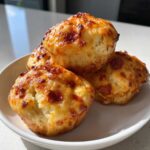 Four freshly baked pizza muffins with melted, slightly browned cheese topping stacked on a small white plate.