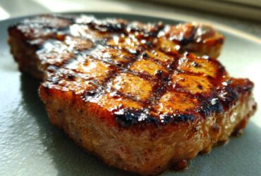 Close-up of a perfectly grilled pork chop showing deep grill marks and a glossy, caramelized exterior from the marinade for pork chops.