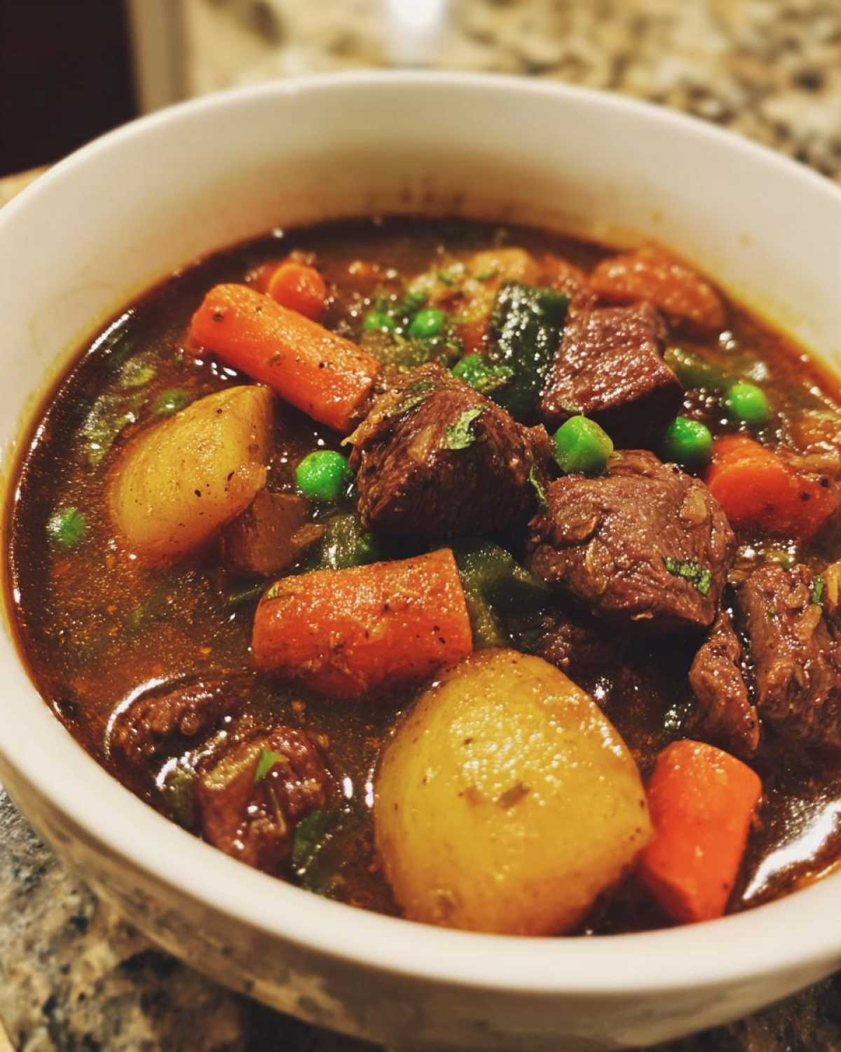 Close-up of a rich, dark broth vegetable beef soup filled with chunks of beef, carrots, potatoes, and peas.