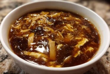 Close-up of a steaming bowl of rich, dark brown hot and sour soup recipe with ribbons of egg and mushrooms.