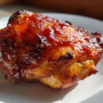 Close-up of a single piece of juicy bbq chicken covered in a thick, glossy, caramelized sauce.
