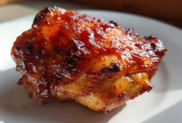 Close-up of a single piece of juicy bbq chicken covered in a thick, glossy, caramelized sauce.