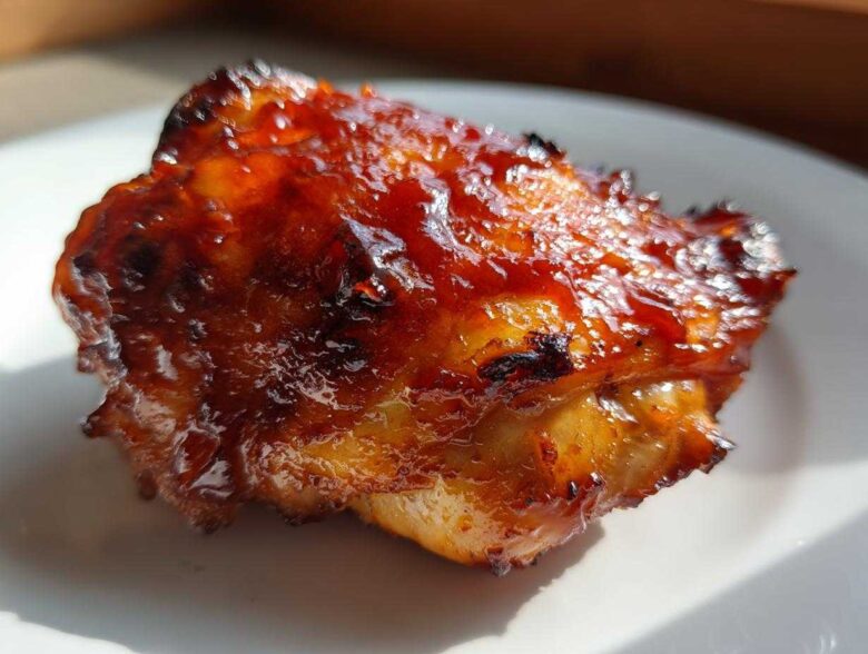 Close-up of a single piece of juicy bbq chicken covered in a thick, glossy, caramelized sauce.