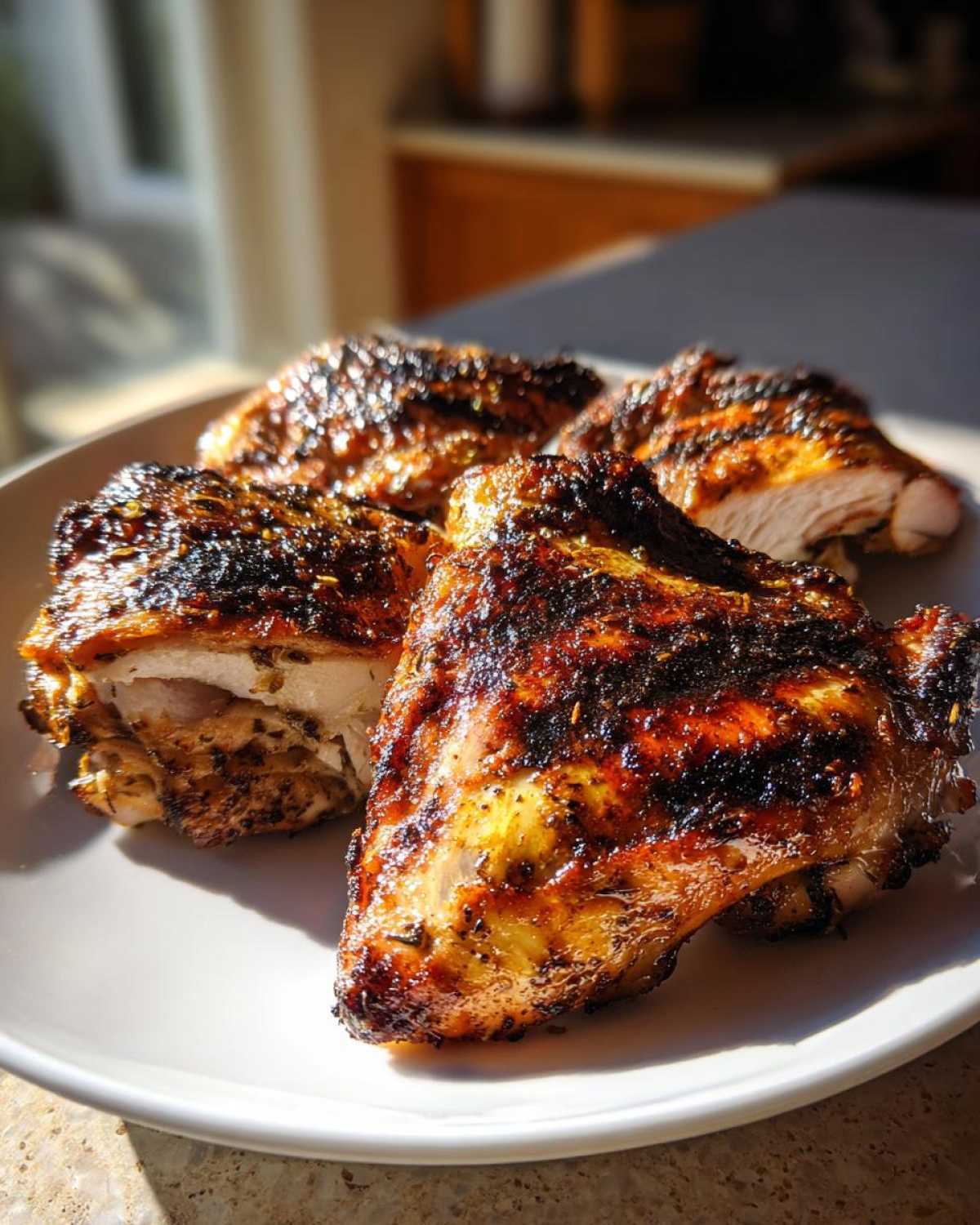 Close-up of perfectly cooked, charred greek chicken thighs resting on a white plate, showing juicy interior.