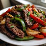 Close-up of juicy steak fajitas featuring sliced steak, red and green bell peppers, and caramelized onions.