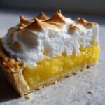 Close-up of a slice of lemon meringue showing bright yellow curd, flaky crust, and perfectly torched meringue.