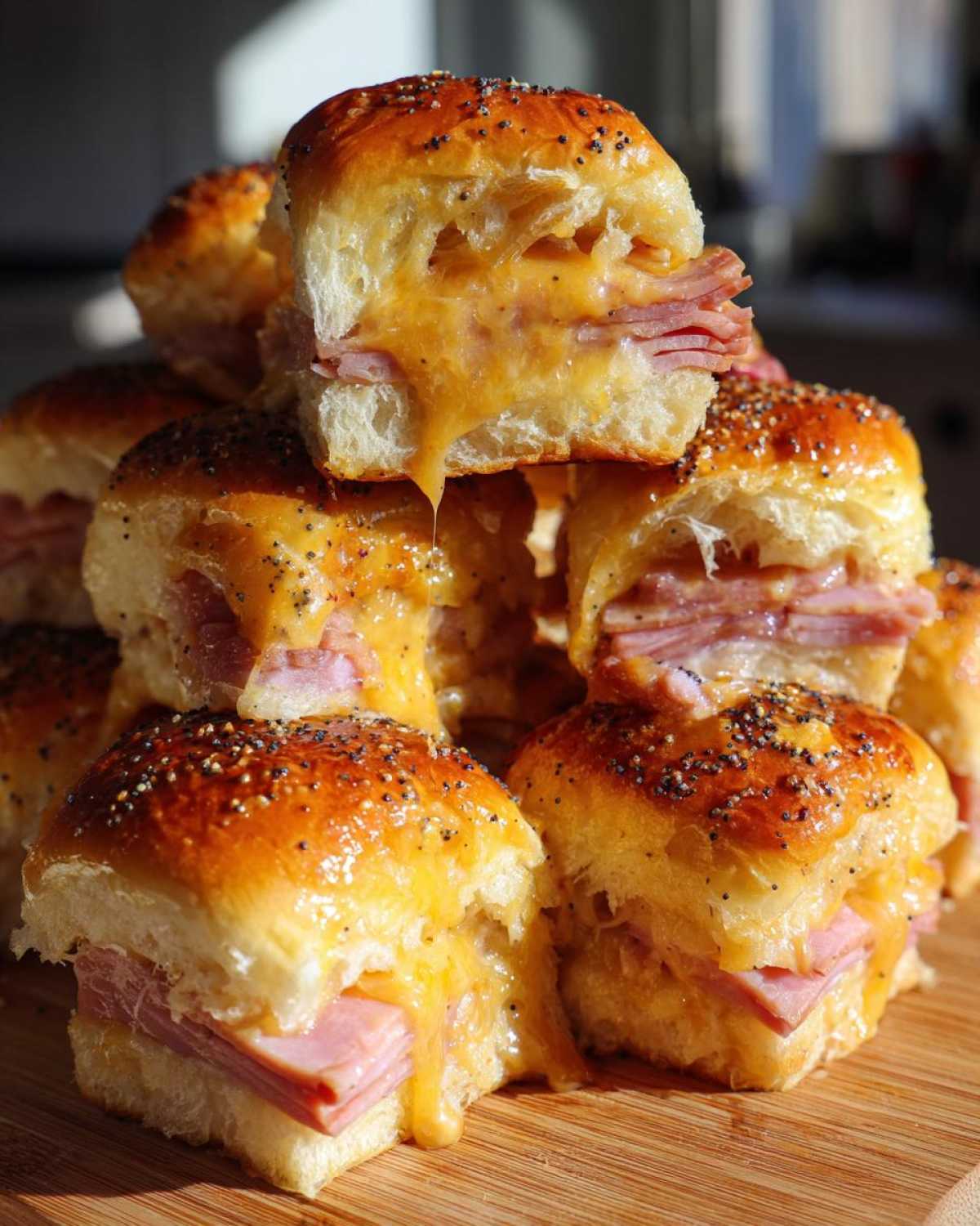 A stack of freshly baked Ham and Cheese Sliders with melted cheese oozing out, topped with poppy seeds.