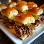 Close-up of several delicious mississippi pot roast sliders piled high with shredded beef and pickles on a white platter.