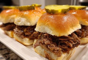 Close-up of several delicious mississippi pot roast sliders piled high with shredded beef and topped with a pickle slice.
