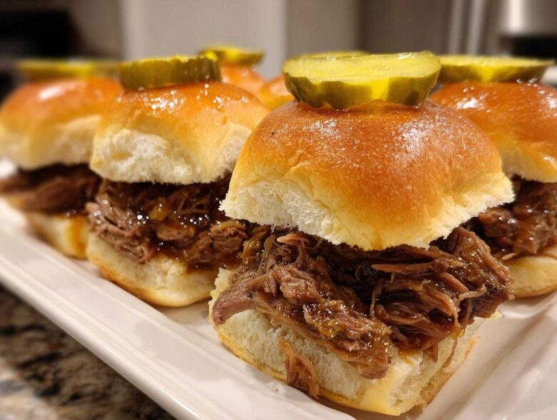 Close-up of several delicious mississippi pot roast sliders piled high with shredded beef and topped with a pickle slice.