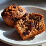 Close-up of a moist bran muffin cut in half, showing the texture and raisins, next to a whole bran muffin.