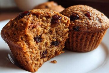 Close-up of a moist bran muffin cut in half showing raisins inside, next to a whole bran muffin.