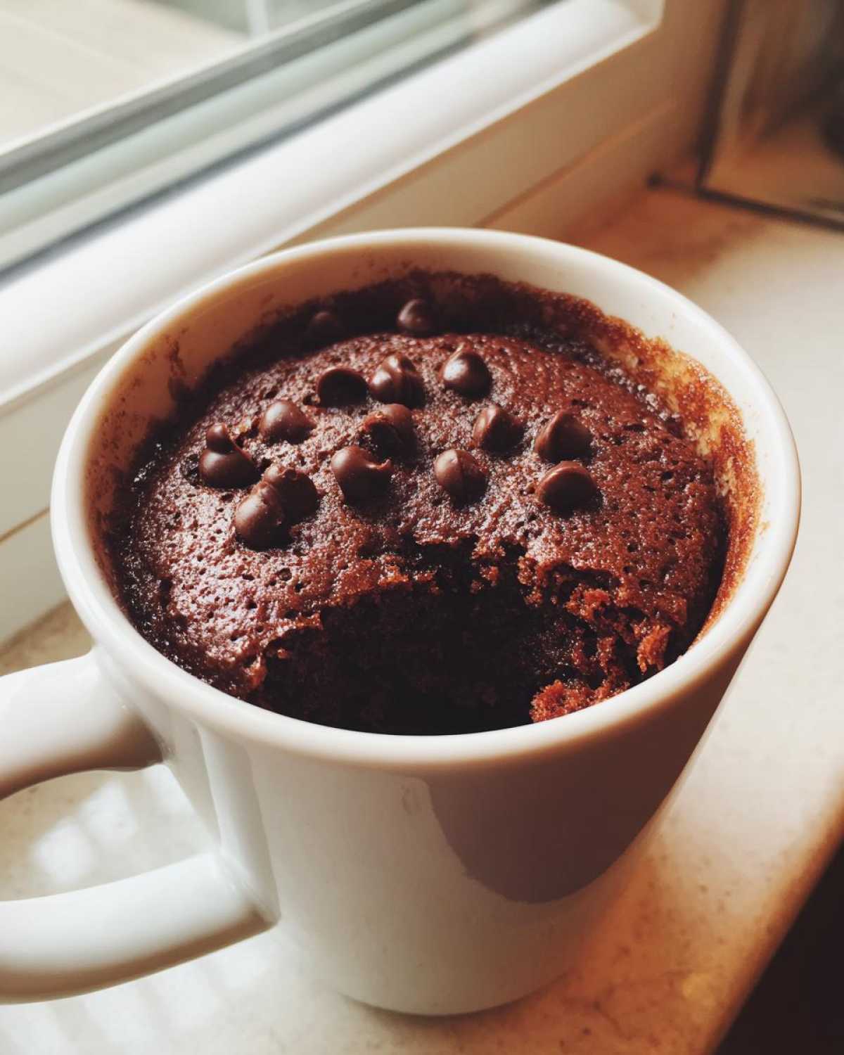 Close-up of a freshly baked, moist chocolate mug cake topped with chocolate chips, with a bite taken out.