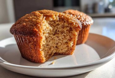 Close-up of a moist honey bran muffin with a bite taken out, showing the crumb texture, on a white plate.