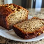 Close-up of a moist sugar free banana bread loaf, partially sliced, showing walnuts on top and a rich crumb texture.