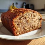 Close-up of a moist slice of sugar free banana bread studded with walnuts, sitting on a white plate.