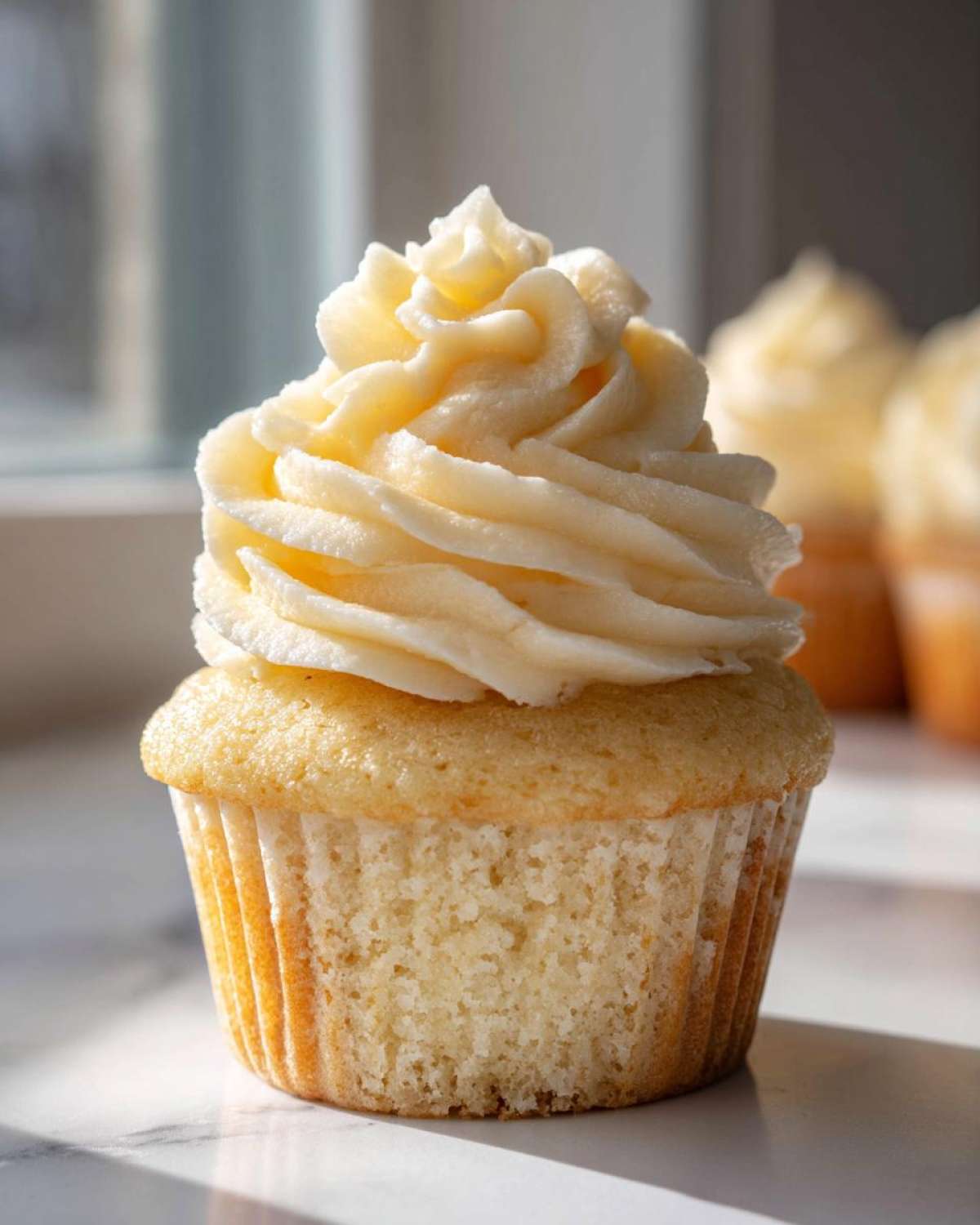 A close-up of one moist vanilla cupcake topped with a swirl of light yellow vanilla buttercream frosting.