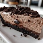 A close-up slice of no-bake Oreo pie featuring a dark chocolate crust and light brown mousse filling.