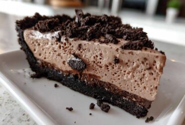 A close-up slice of no-bake Oreo pie featuring a dark chocolate crust and light brown mousse filling.