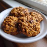A close-up of four textured oatmeal chocolate chip breakfast cookie treats on a white plate.