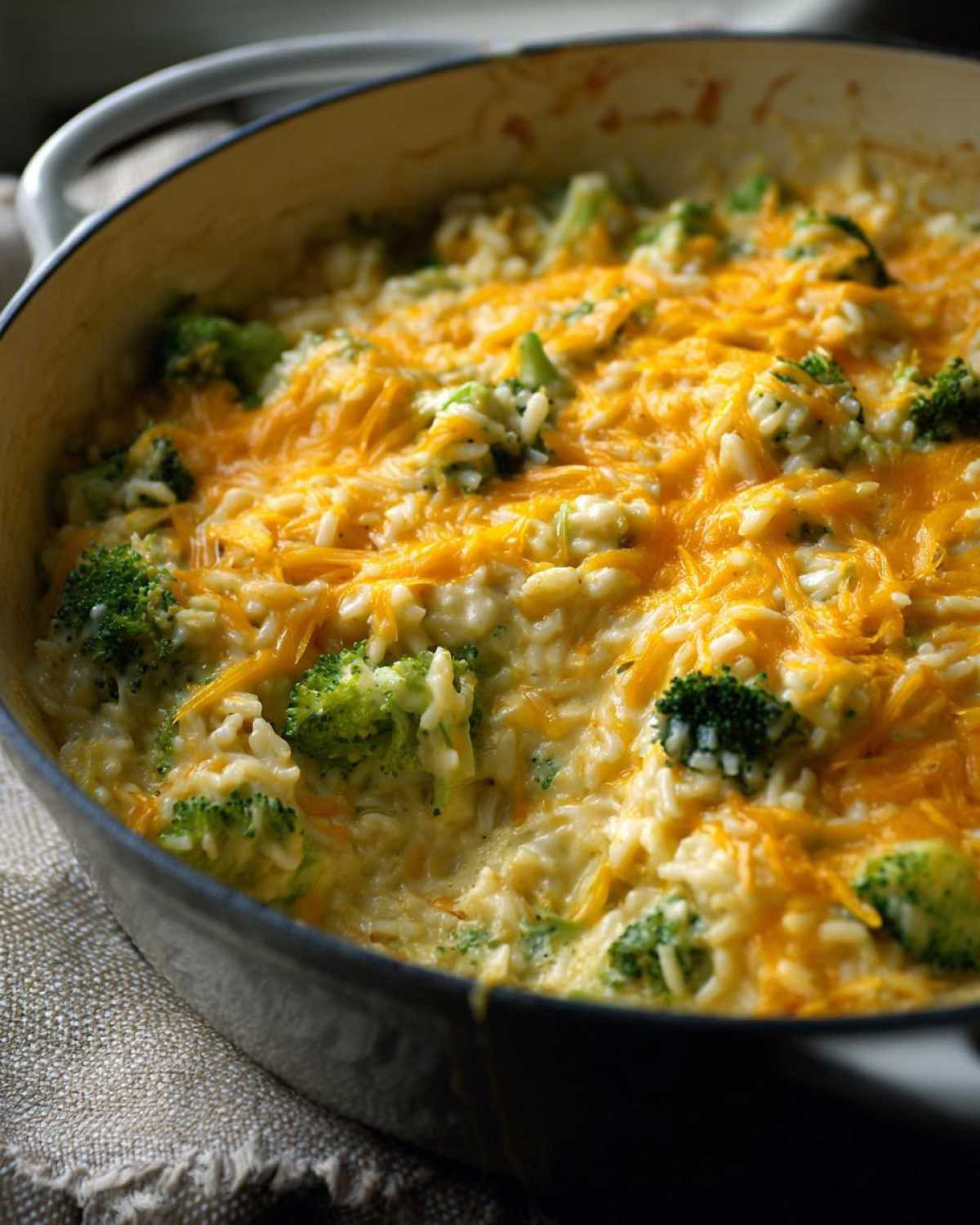 Close-up of creamy, cheesy broccoli rice topped with melted cheddar cheese in a cast iron pot.