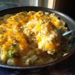 Close-up of creamy, cheesy broccoli rice in a skillet, with a spoonful being lifted out.