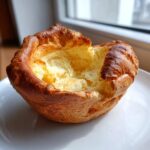 A single, perfectly risen yorkshire pudding with a golden-brown crust and a hollow center, sitting on a white plate.