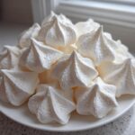 A white plate piled high with freshly piped, star-shaped meringue cookies, ready to eat.