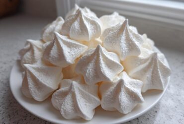 A white plate piled high with freshly piped, star-shaped meringue cookies, ready to eat.