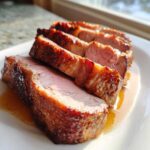 Close-up of juicy, medium-rare pork loin roast slices with a beautifully seared, glazed crust resting in pan juices.